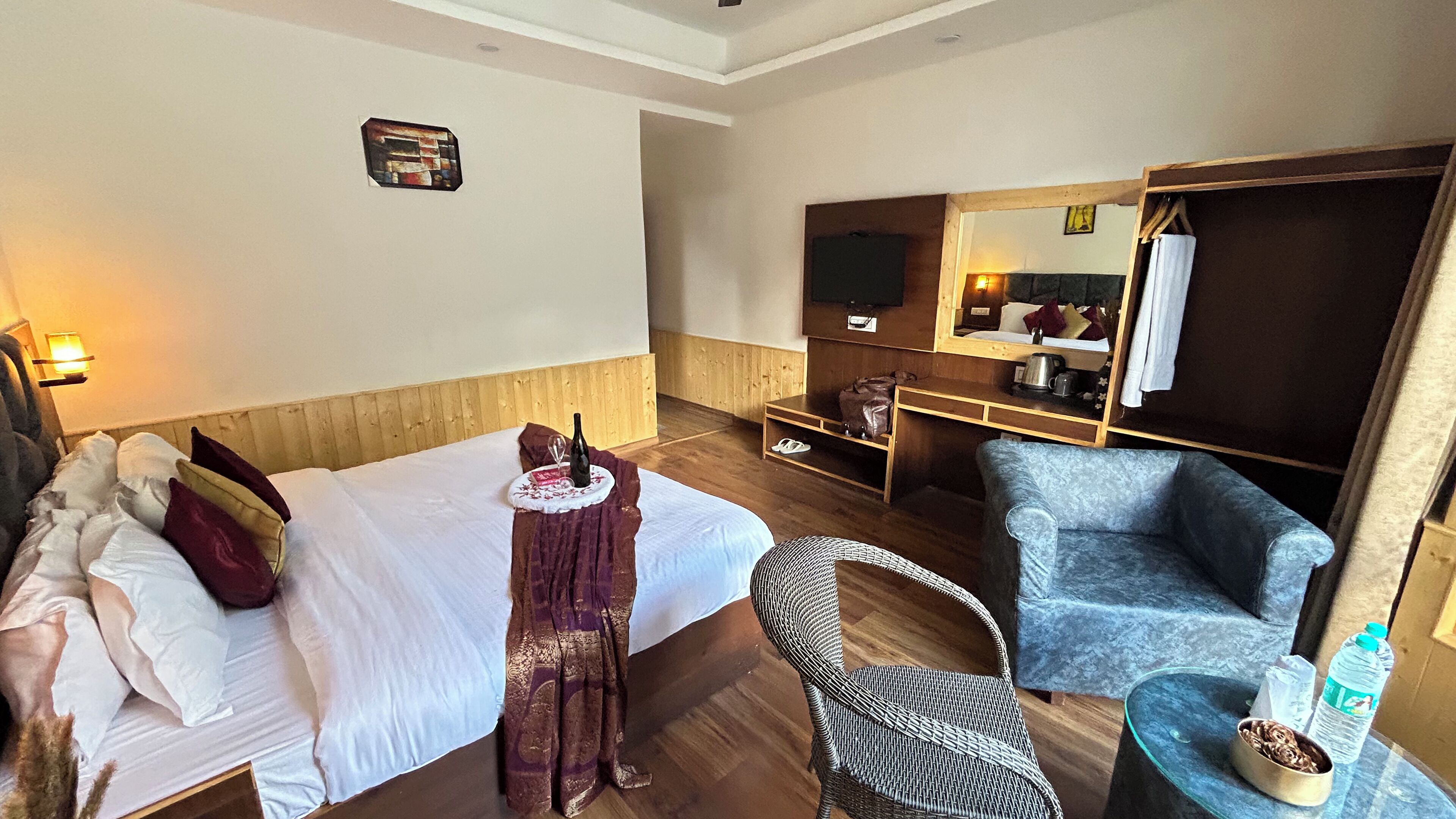 Une chambre d’hôtel avec un lit, une chaise, une petite table, un miroir et un plancher en bois.