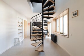 Un interior moderno con una escalera espiral, un comedor y un ventanal con luz natural.