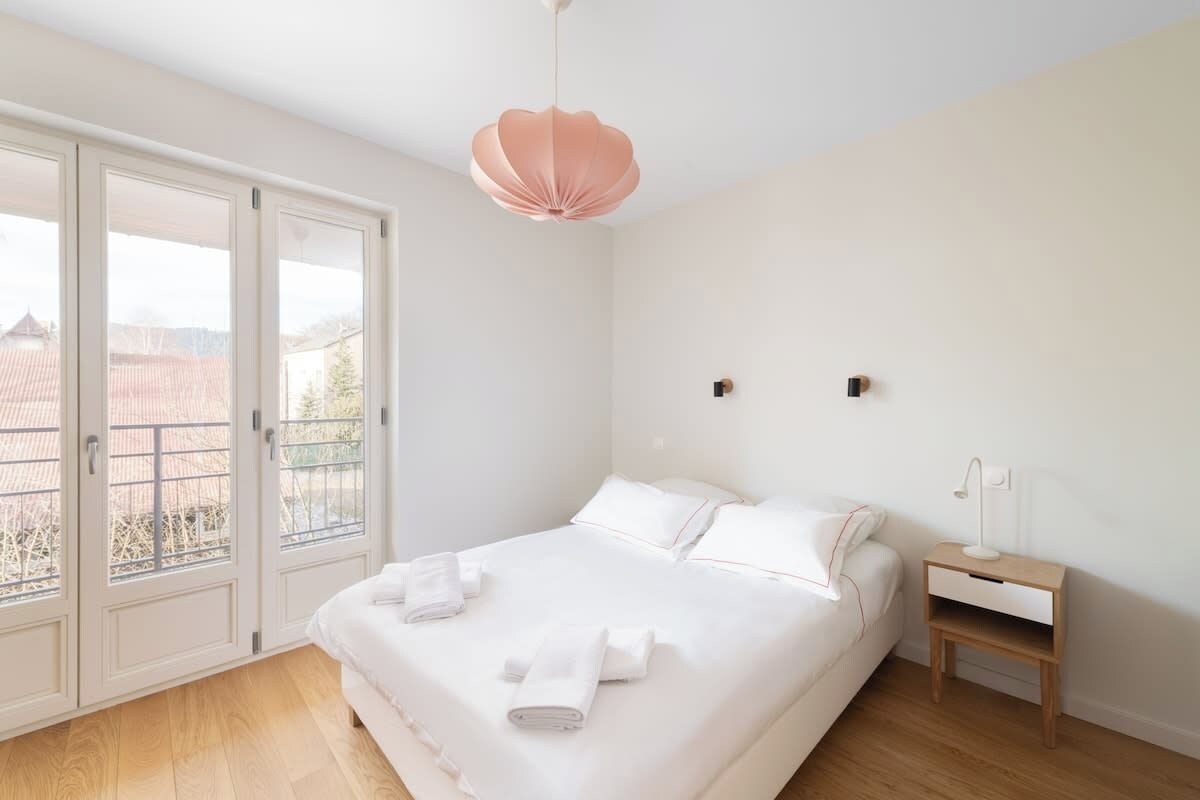 Ein Schlafzimmer mit einem großen Bett, einem Nachttisch, einer Pendelleuchte und Blick durch eine Schiebetür.