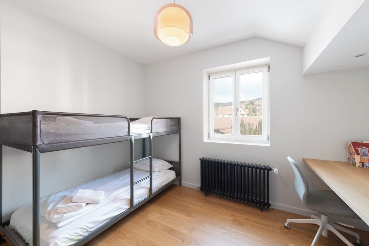 A room with bunk beds, a radiator, a desk with a chair, and a window with a view.