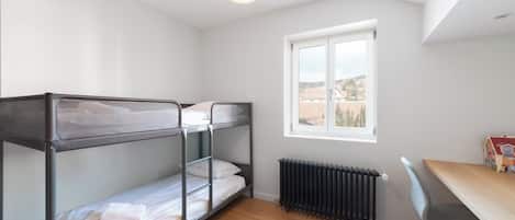 Une chambre avec des lits superposés, un radiateur, un bureau avec une chaise et une fenêtre donnant sur un paysage agréable.
