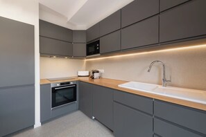 Een moderne keuken met grijze kastjes, een houten aanrechtblad, een ingebouwde magnetron en een roestvrijstalen spoelbak.