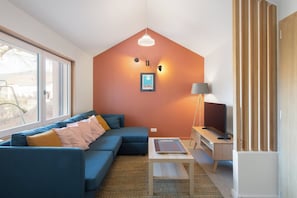 Een moderne woonkamer met een hoekbank, een flatscreen televisie, een bijzettafeltje en een groot raam.