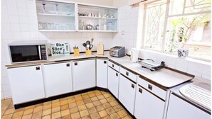 Een keuken met witte kastjes, een magnetron, een broodrooster en een raam met uitzicht op groen.
