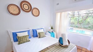 Een hotelkamer met een bed, een raam met uitzicht op groen en drie geweven wanddecoraties.