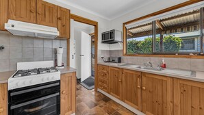 A modern kitchen with wooden cabinets, a gas stove, an oven, a microwave, and a large window with a view of greenery.