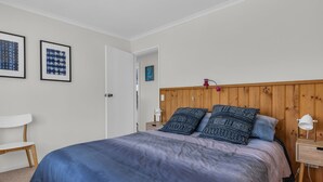 A bedroom with a bed, a nightstand, a chair, and two framed artworks on the wall.