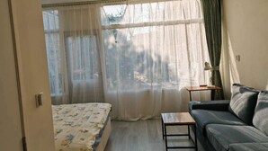 A room with a bed, a sofa, a small table, and a window with sheer curtains. - Studio Breda Modern Furnishing space with a comfortable, 4min drive station. (Breda)