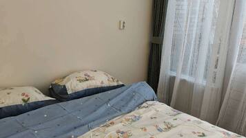 Ein Schlafzimmer mit einem Bett, floralem Bettbezug, einem Fenster mit Vorhängen und einer Steckdose.