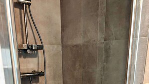 A shower area with a glass door, a handheld showerhead, and a wall-mounted control panel. - Studio Breda Modern Furnishing space with a comfortable, 4min drive station. (Breda)