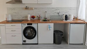 A compact kitchen with a washing machine, a small refrigerator, a sink, and a coffee maker. - Studio Breda Modern Furnishing space with a comfortable, 4min drive station. (Breda)