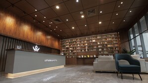 A hotel reception area with a modern design, featuring a reception desk, a large bookshelf filled with books, and a seating area with a sofa and chairs. - LOTUS BLU HOTEL NAGA (Naga)