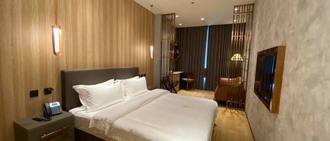 A modern hotel room with a large bed, bedside table with a phone, and a TV mounted on the wall.