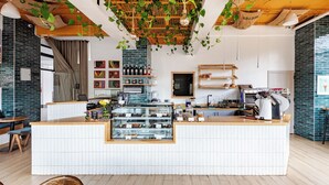 Un café moderno con mostrador de madera, salpicadero de azulejos blancos y plantas colgantes.