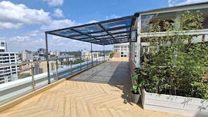 A rooftop terrace with a glass enclosure, potted plants, and a view of the cityscape.