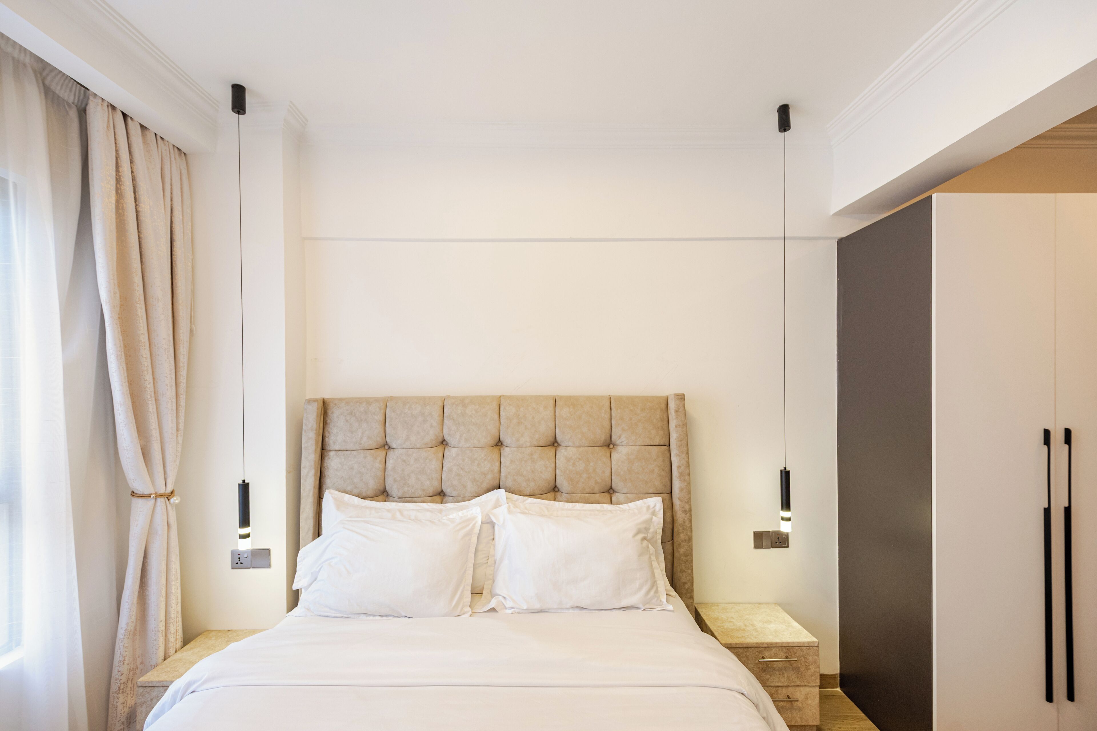 Quarto moderno com cabeceira estofada, mesa de cabeceira e guarda-roupa.