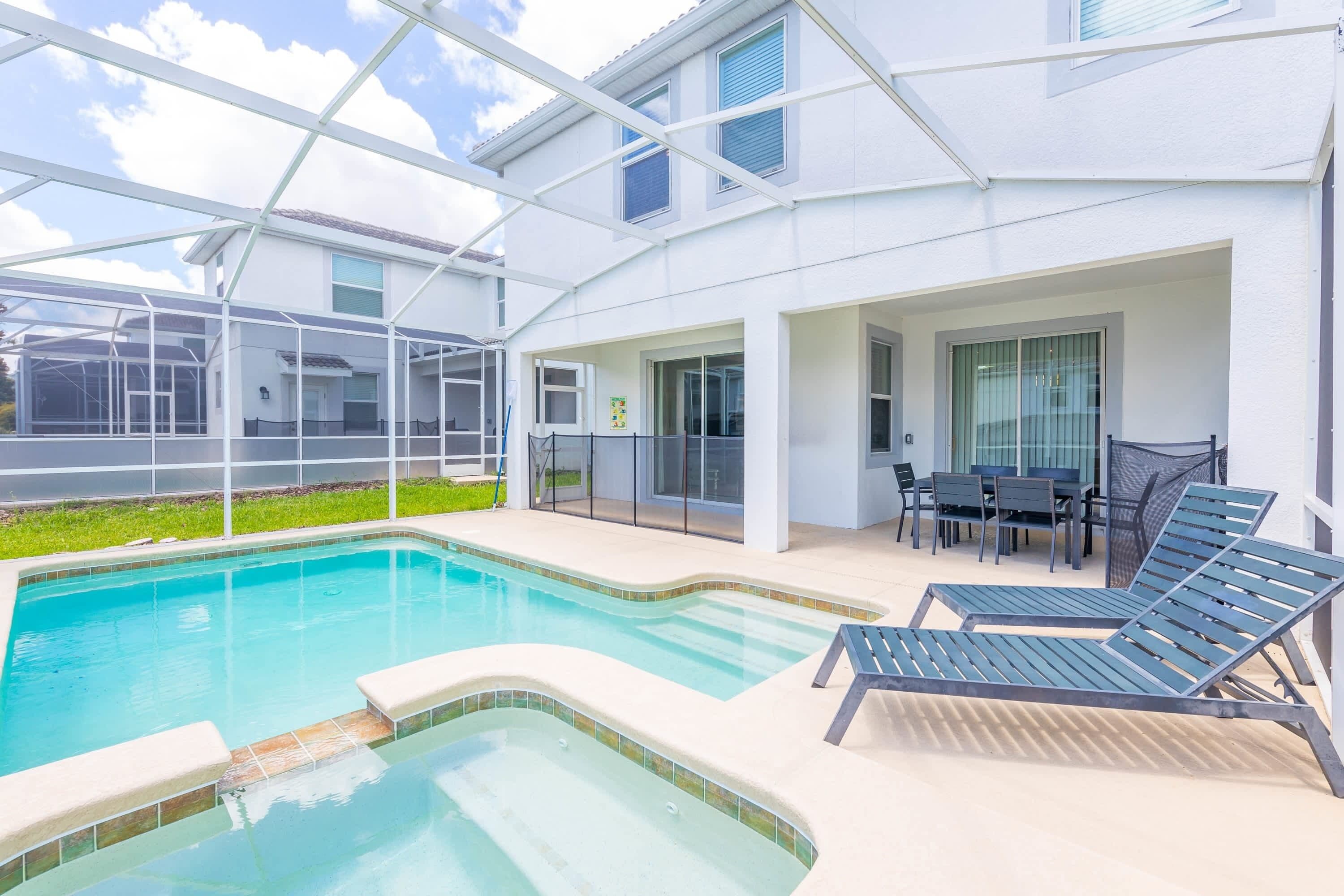 A modern outdoor pool area with lounge chairs, a covered patio, and a glass-enclosed structure.