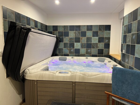 A bathroom with a hot tub, tiled walls, a towel rack, and a wooden chair. - Bed and breakfast with private Jacuzzi in secluded countryside setting. Relaxation guaranteed! (Fresnes)