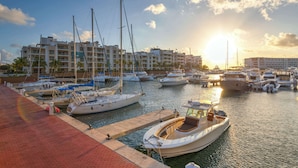 Un puerto deportivo con barcos amarrados, un paseo marítimo y un conjunto de edificios al fondo.