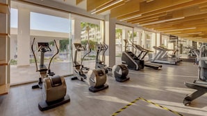 A modern gym with various exercise equipment, large windows, and a wooden ceiling. - Beach Club Access & Rooftop Pool in La Amada (Cancún)