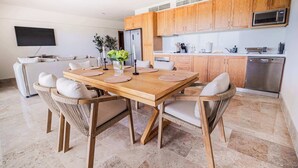 A modern kitchen with wooden cabinets, a dining table with chairs, and a built-in microwave. - Beach Club Access & Rooftop Pool in La Amada (Cancún)