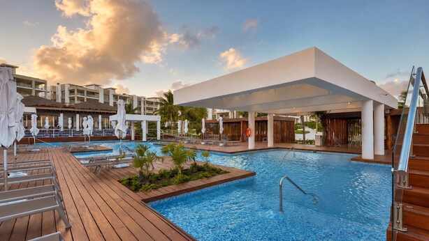 A swimming pool with a wooden deck, lounge chairs, and umbrellas. - Beach Club Access & Rooftop Pool in La Amada (Cancún)