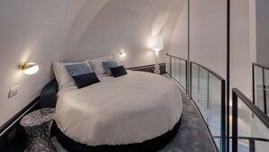 A modern bedroom with a curved ceiling, a large bed, bedside lamps, and a glass railing.