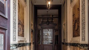 A hallway with a red carpet, marble walls, and a chandelier.