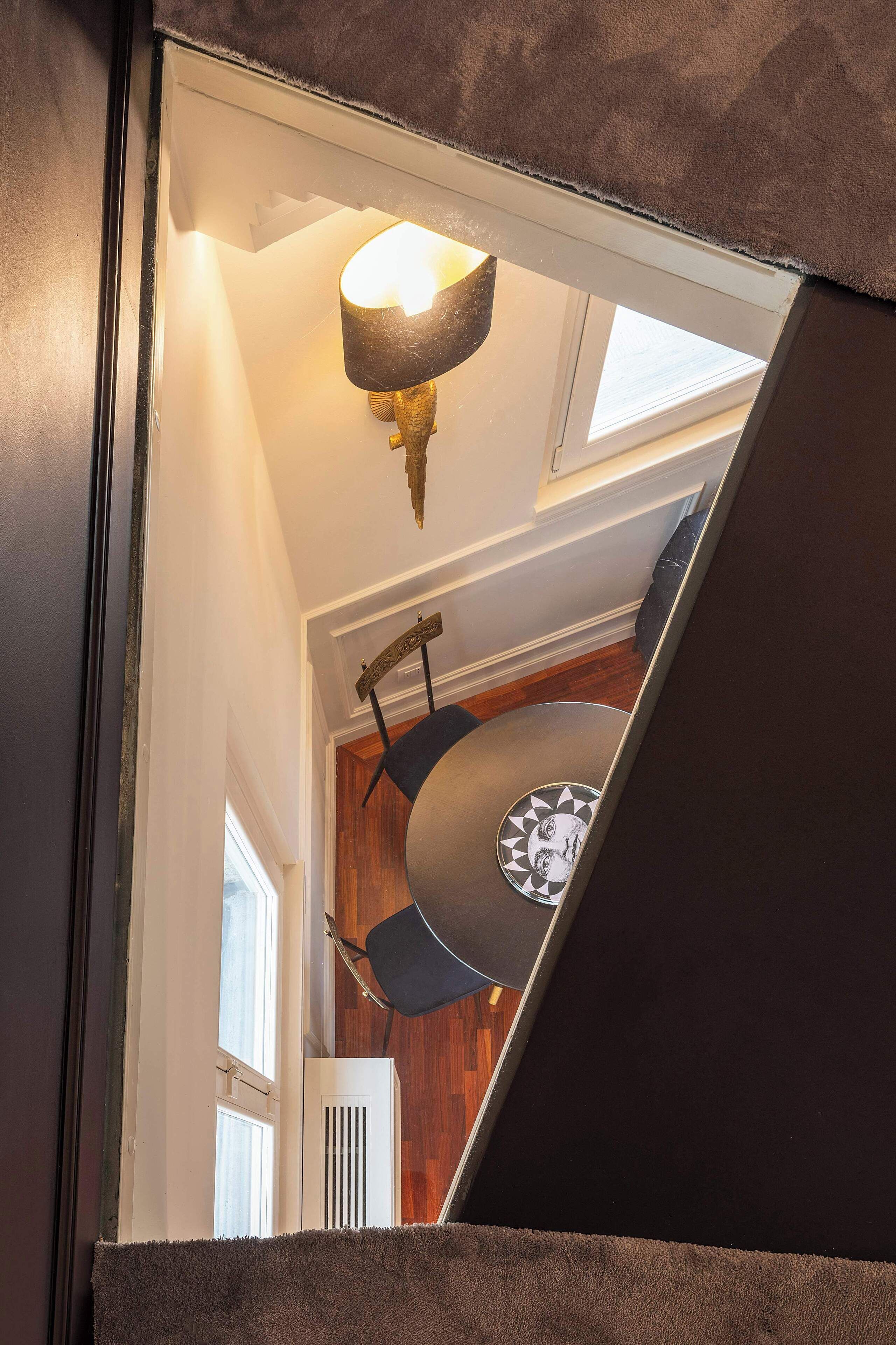 Una escalera con una pared oscura, un accesorio de luz en el techo y una ventana con persianas.