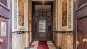 A grand hallway with marble walls, a red carpet, and a large wooden door with a glass panel.