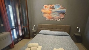 A bedroom with a bed, two bedside tables, a nightstand, a window with curtains, and a wall with a sunset painting. - Apartment within walking distance of the Politeama Theater on Principe di Belmonte Street (Palermo)