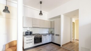 A modern kitchen with light-colored cabinets, a microwave, stove, and oven. There is a wooden chair and a pendant light.