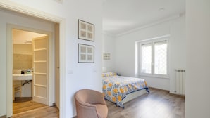A bedroom with a bed, a chair, a window, and a bathroom visible through an open door.