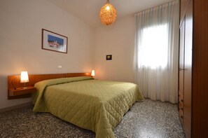 A hotel room with a bed, two bedside lamps, a picture on the wall, a chandelier, and a window with curtains. - Comfy holiday retreat with balcony near the beach (Bibione Pineda)