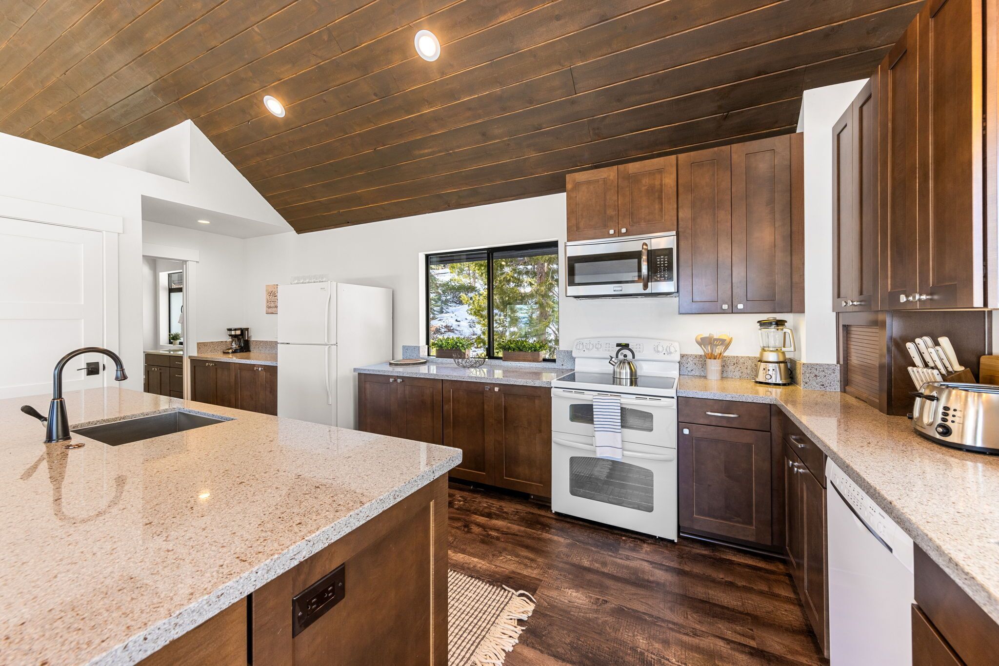 A modern kitchen with wooden cabinets, a granite countertop, stainless steel appliances, and a large window providing natural light.