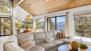 Un salon moderne doté d’un grand canapé d’angle, d’un plafond en bois et de grandes fenêtres offrant une vue sur les montagnes.