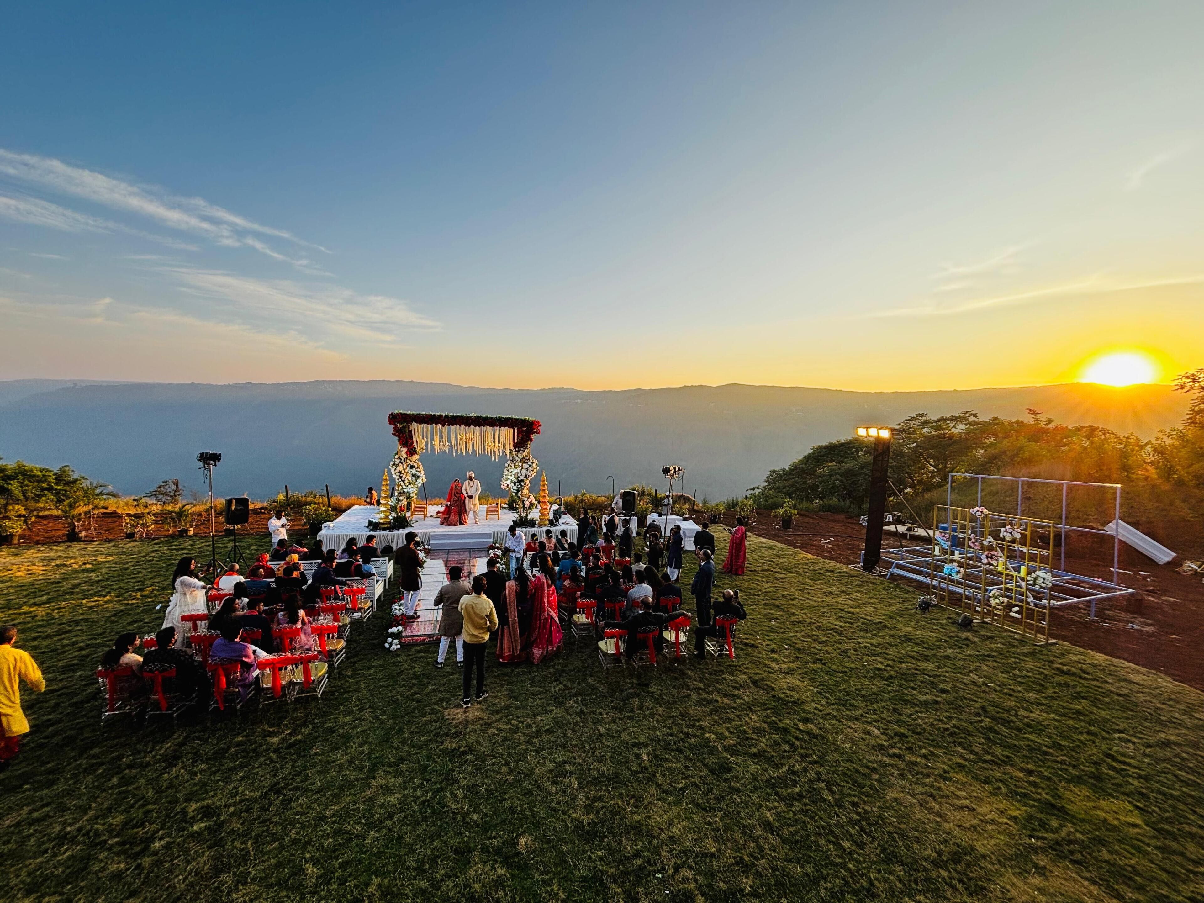 Una ceremonia de boda en una colina cubierta de césped, con vista despejada al atardecer y montañas distantes.