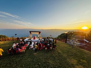 A wedding ceremony on a grassy hill with a clear view of the sunset and distant mountains. - MOUNTAIN BREEZE RESORT (Mahabaleshwar)