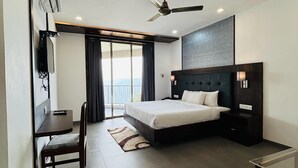 A modern hotel room with a large bed, a desk, a chair, and a ceiling fan. - MOUNTAIN BREEZE RESORT (Mahabaleshwar)