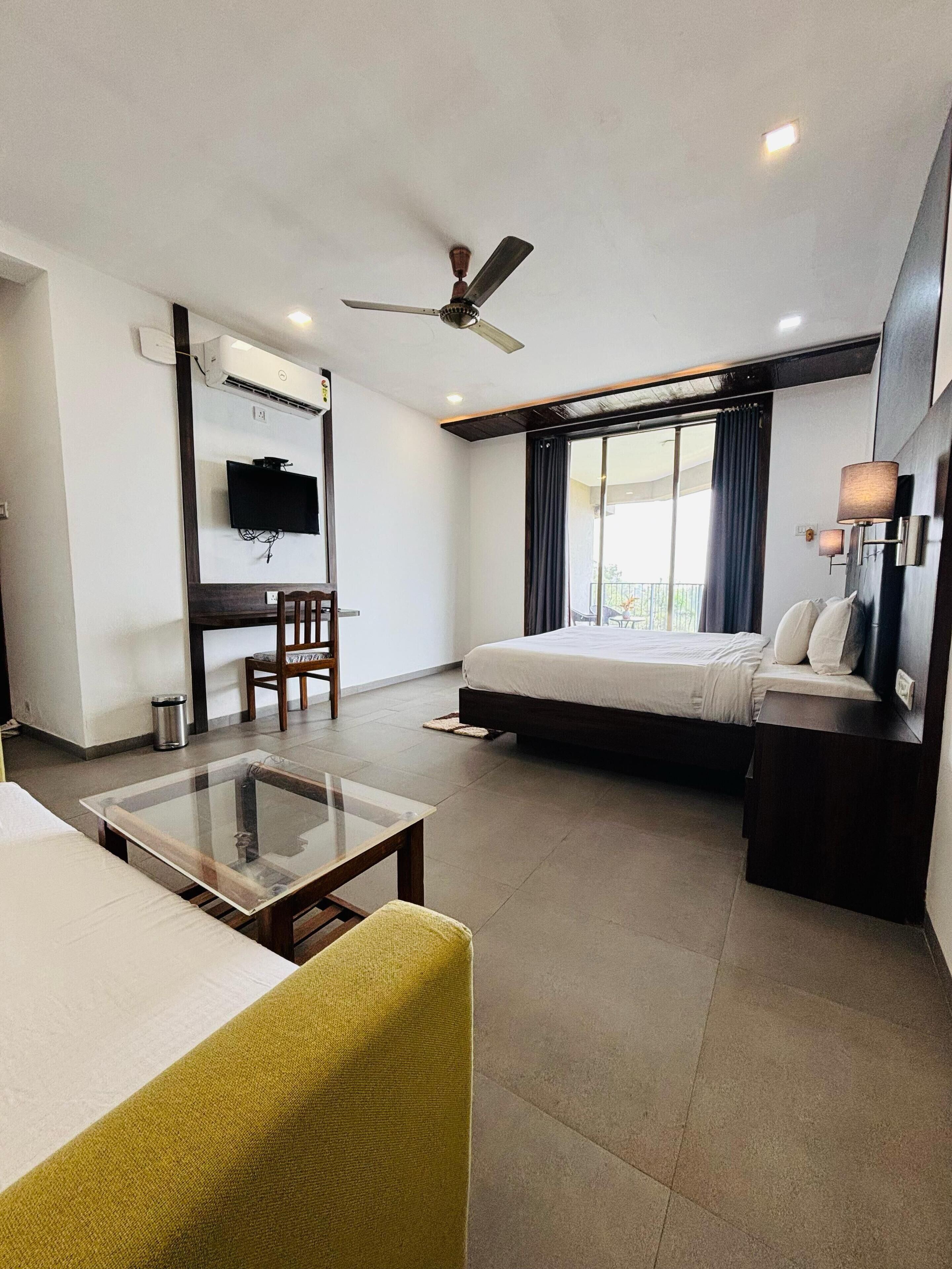 Une chambre d’hôtel moderne équipée d’un lit, d’un bureau, d  ’une chaise, d’une télévision et d’un balcon avec des rideaux.