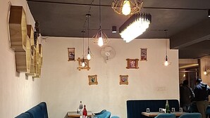 A restaurant interior with blue seating, wooden tables, and geometric pendant lighting. - MOUNTAIN BREEZE RESORT (Mahabaleshwar)