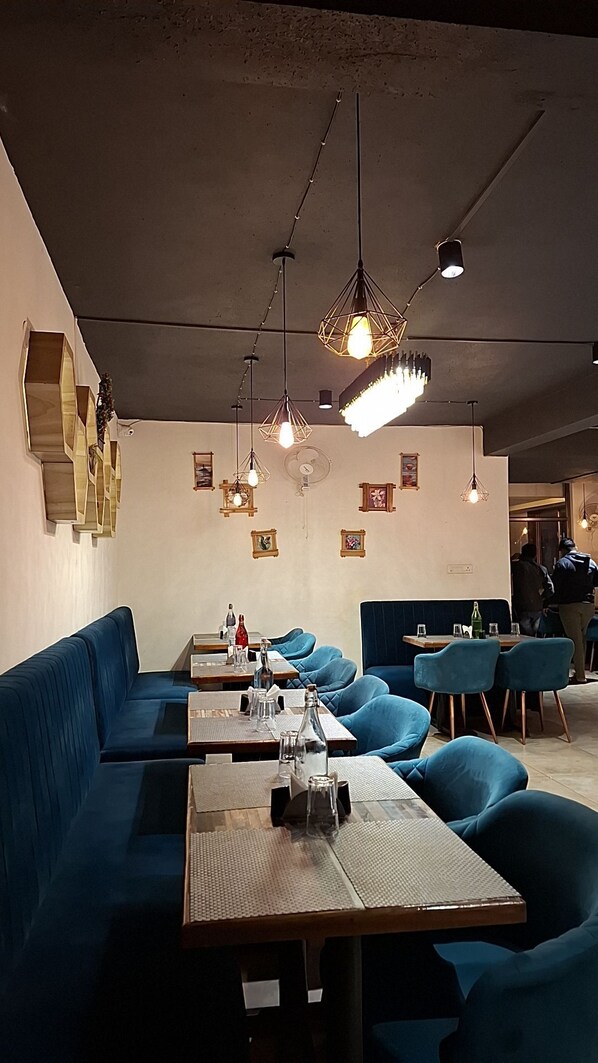 A restaurant interior with blue seating, wooden tables, and geometric pendant lighting.