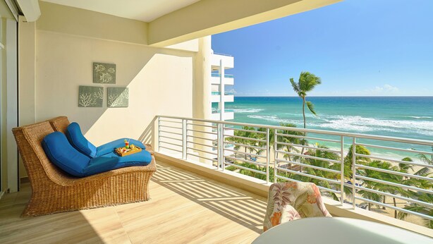 Un balcon avec un canapé en osier, une petite table avec un plateau, et une vue sur l’océan et la plage.