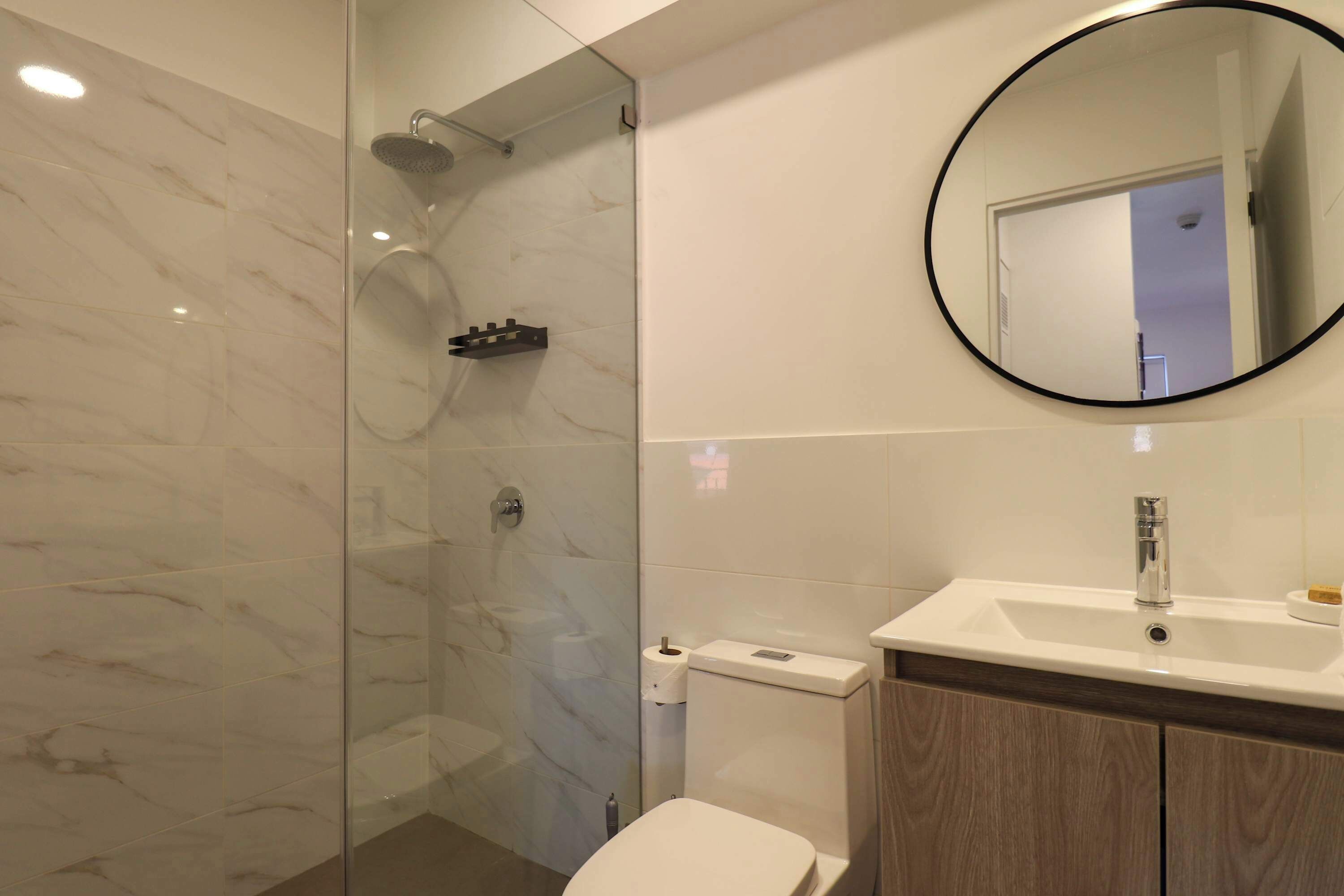 A bathroom with a glass-enclosed shower, a toilet, a sink, and a mirror.