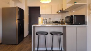 Une cuisine moderne équipée d’un réfrigérateur en acier inoxydable, d’un four à micro-ondes et d’un comptoir-bar avec deux tabourets.