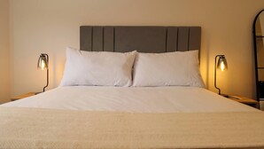 A neatly made bed with a grey headboard, two bedside lamps, and a beige throw blanket. - w* | Modern 2BR in Historic Cusco w/ Balcony (Cusco)