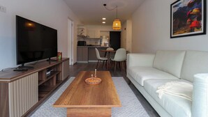 A modern living room with a flat-screen TV, wooden coffee table, white sofa, and a dining area with chairs and a table. - w* | Modern 2BR in Historic Cusco w/ Balcony (Cusco)
