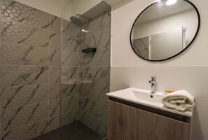 Ein Badezimmer mit Marmor-Duschwand, einem runden Spiegel und einem Waschbecken mit Handtuch.