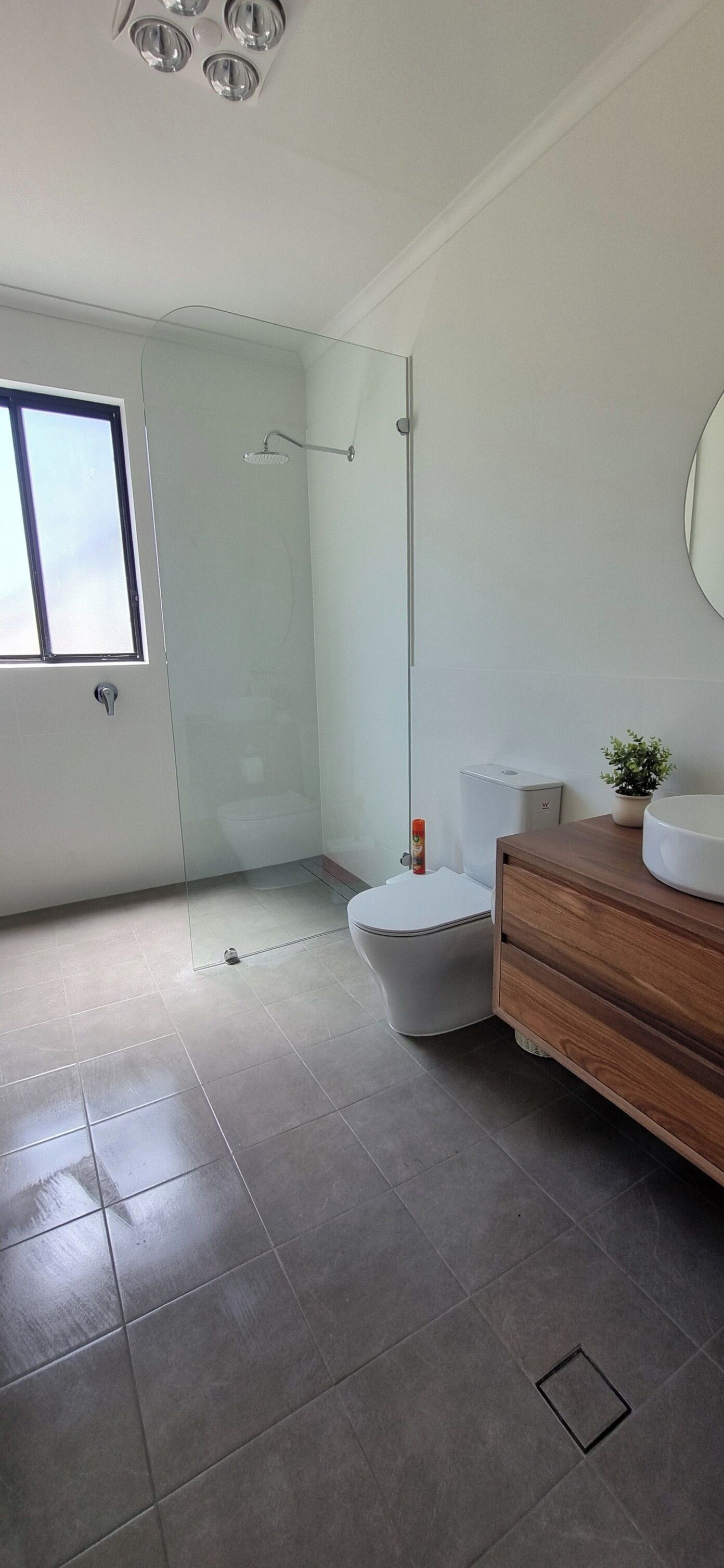 A modern bathroom with a glass shower enclosure, a toilet, and a wooden vanity with a sink.