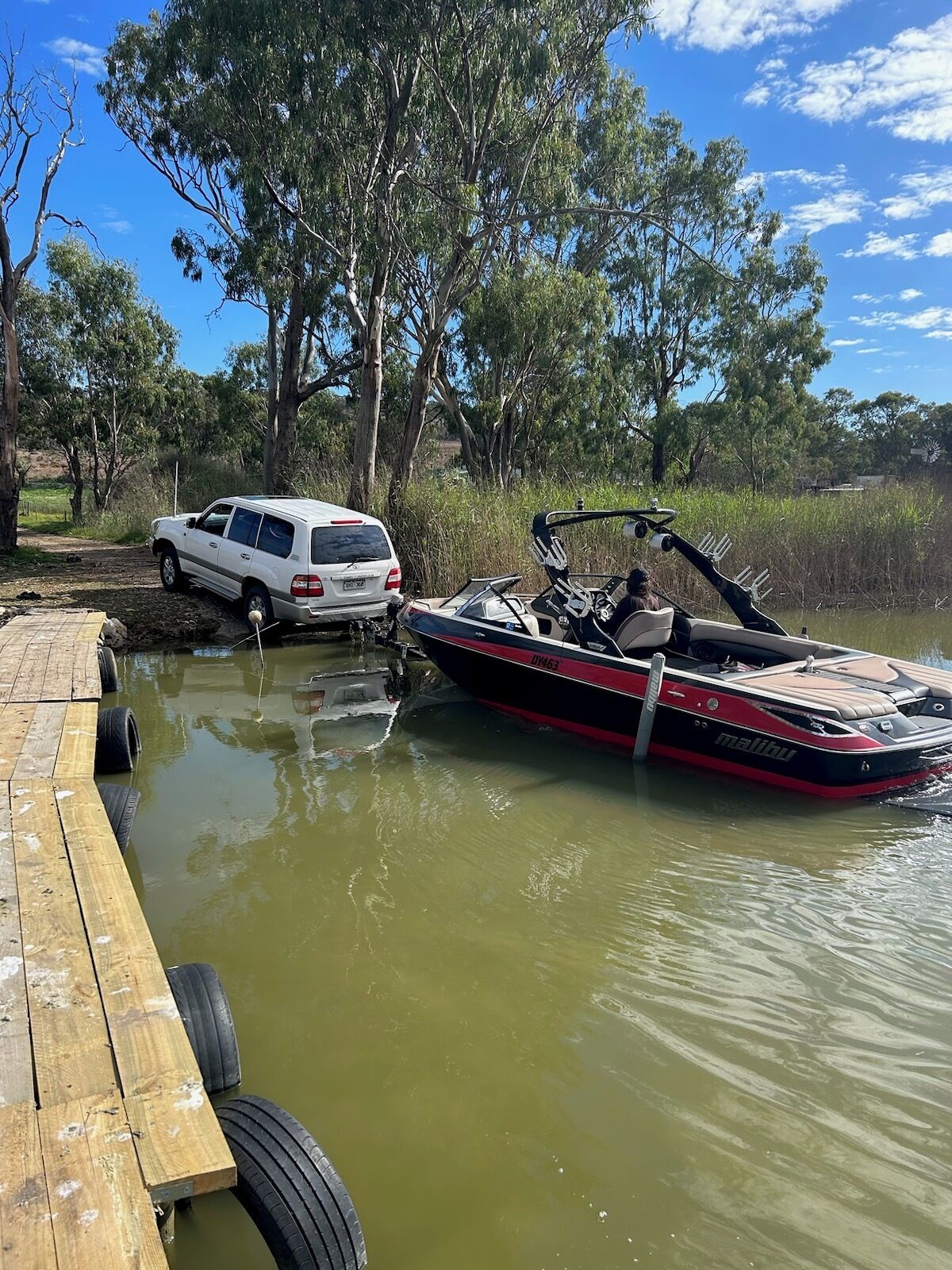 A boat docked at a wooden pier with a white vehicle nearby.